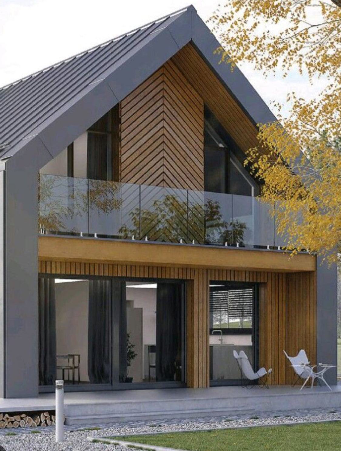 Modern two-story house exterior with a steep gray metal roof, wood-paneled walls, large glass windows, a glass balcony railing, and a landscaped lawn with a tree in the foreground.